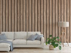 a white couch sitting in front of a wooden wall next to a lamp and plant