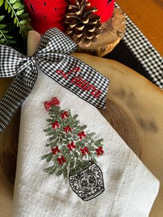 an embroidered christmas tree on a white dish towel next to a pine cone and red berries