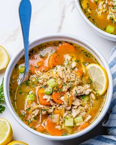 two bowls filled with chicken and vegetable soup next to sliced lemons on a white surface