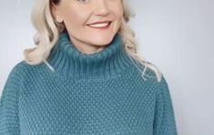 a woman with blonde hair wearing a blue turtle neck sweater and smiling at the camera