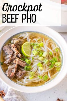 a bowl of beef pho soup with noodles and sliced limes on the side