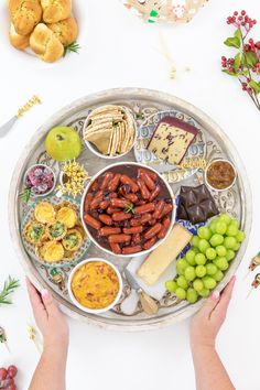 two hands holding a platter full of snacks and fruit on a white tablecloth