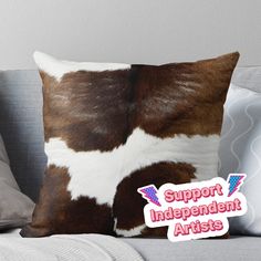 a brown and white cow print pillow sitting on top of a couch with the words support independent artists