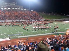 an orange and white marching band performing on a football field in front of a large crowd