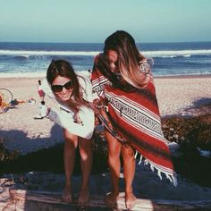 two young women standing on the beach with their arms around each other, wrapped in blankets