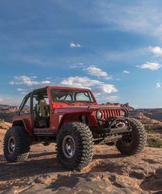 a red jeep is parked on top of a rock outcropping in the desert