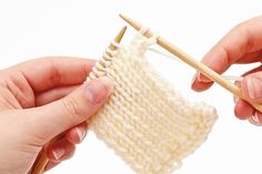 two hands holding knitting needles over a white knitted object