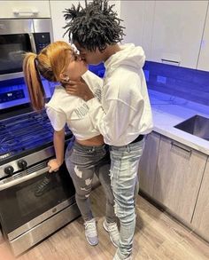 two people standing in front of an oven with their backs to each other and kissing