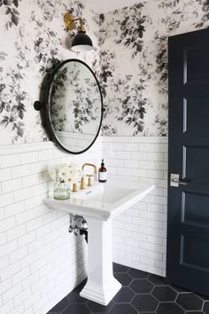 the bathroom is decorated with black and white floral wallpaper, gold faucets, and a round mirror