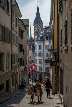 people walking down an alley way with buildings and a clock tower in the background