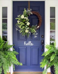 a blue front door with a wreath on it and two plants in the foreground