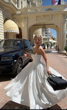 a woman in a white dress is walking down the street with her hand on her purse