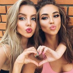 two beautiful young women making heart shapes with their hands