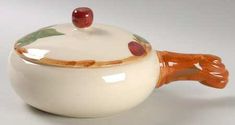 a ceramic tea pot with an orange handle and red fruit on the top, sitting in front of a white background