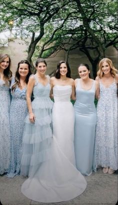 a group of women in dresses standing next to each other on a sidewalk with trees behind them