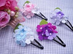 three hair pins with flowers on them sitting next to some pink and purple flowers in the background