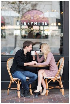 a man and woman sitting at a table in front of a store window drinking coffee