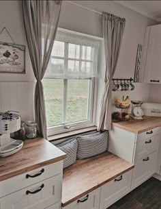 a kitchen with white cabinets and wooden counter tops next to a large window in the corner