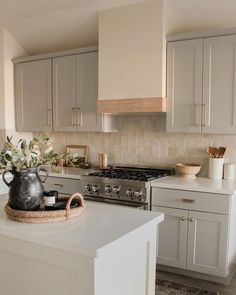 a kitchen with white cabinets and an island in front of a stove top oven, potted plant on the counter