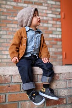 a little boy sitting on top of a brick wall wearing jeans and a knitted hat