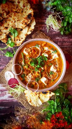 a bowl filled with soup next to some pita bread and garnishes