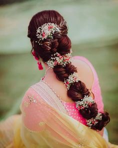 a woman with braids and flowers in her hair is wearing a pink sari