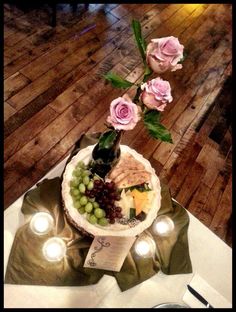 a table topped with a cake covered in cheese and grapes next to flowers on top of a wooden floor