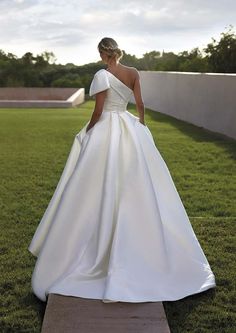 a woman in a white wedding dress standing on the grass with her back to the camera