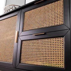 a black cabinet with some gold handles on the front and side panels that are made out of rattan