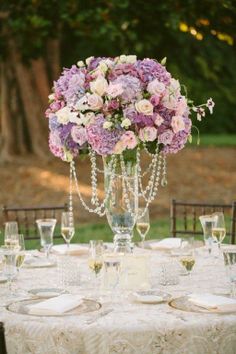 the centerpieces on this table are filled with purple and white flowers, which is surrounded by crystalware