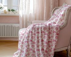 a chair with a pink flowered blanket draped over it's back in front of a window