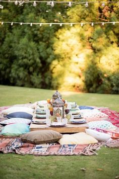 an outdoor picnic with pillows, plates and tea kettle on the grass in front of trees