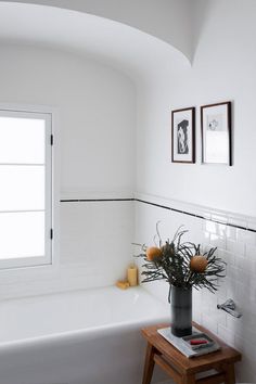 a white bath tub sitting under a window next to a wooden table with flowers in it