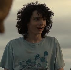 a woman with curly hair standing in front of a man wearing a t - shirt