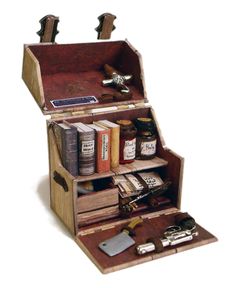 an open wooden box filled with lots of books and writing utensils on top of a white surface