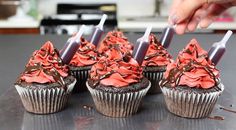 chocolate cupcakes with red frosting and sprinkles are being cut