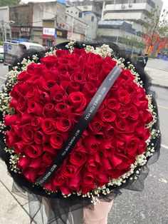 a person holding a large bouquet of red roses on the side of the road with buildings in the background