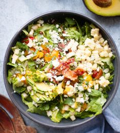 a bowl filled with salad next to an avocado on top of a table