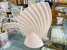 a white shell shaped vase sitting on top of a glass table next to chairs and tables