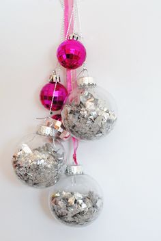 three ornaments hanging from a pink ribbon on a white wall with silver and pink decorations