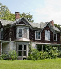 an old, run down house sits in the middle of a grassy area with trees and bushes around it