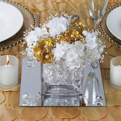 a vase filled with white and gold flowers on top of a table next to candles