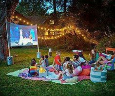 a group of people sitting on top of a lush green field next to a movie screen