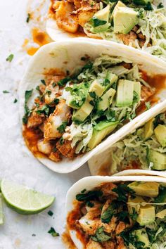 three fish tacos with avocado, cilantro and lime wedges