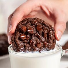 a person is holding a chocolate cookie in a glass of milk