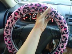 a person is driving in a car with pink leopard print steering wheel cover on the dashboard