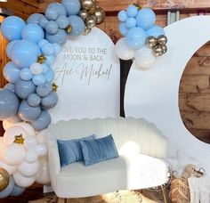 balloons are hanging from the ceiling in front of a white couch and chair with blue pillows