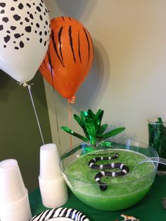 a table topped with plates and balloons filled with green liquid next to a bowl full of food