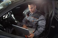 a man sitting in the driver's seat of a car using a laptop computer