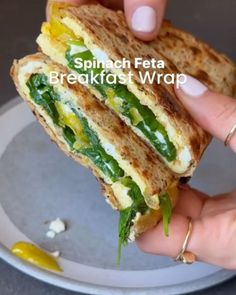 a person is holding a sandwich with spinach and feta cheese on it in front of a plate